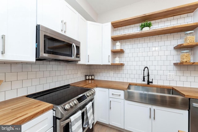 kitchen featuring butcher block countertops, backsplash, appliances with stainless steel finishes, sink, and white cabinets