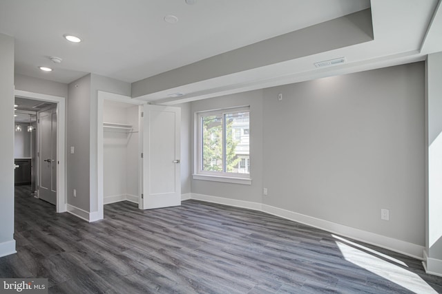 unfurnished bedroom featuring a closet, dark wood-type flooring, and a walk in closet