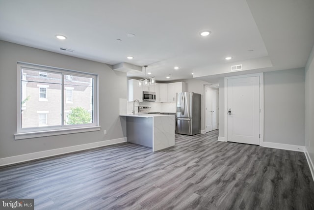 kitchen with appliances with stainless steel finishes, white cabinetry, kitchen peninsula, wood-type flooring, and a chandelier