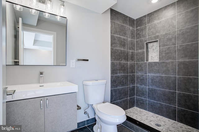 bathroom with tile patterned flooring, tiled shower, vanity, and toilet