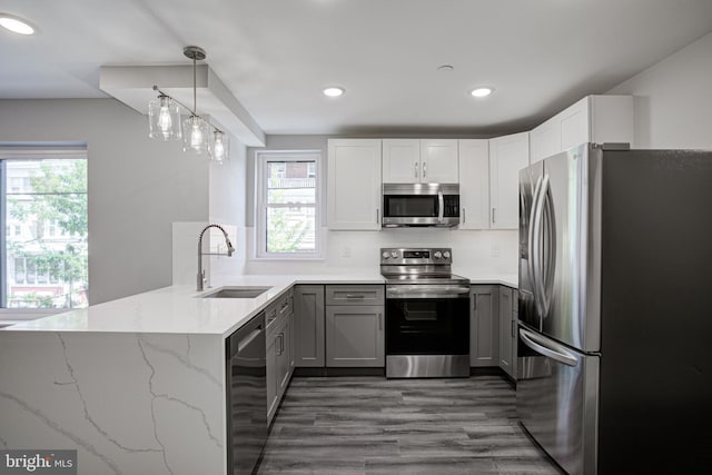 kitchen featuring hanging light fixtures, sink, kitchen peninsula, appliances with stainless steel finishes, and light stone countertops