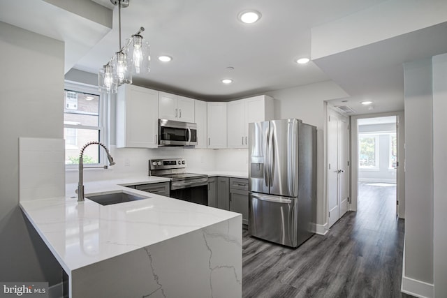 kitchen featuring appliances with stainless steel finishes, white cabinets, light stone countertops, decorative light fixtures, and sink