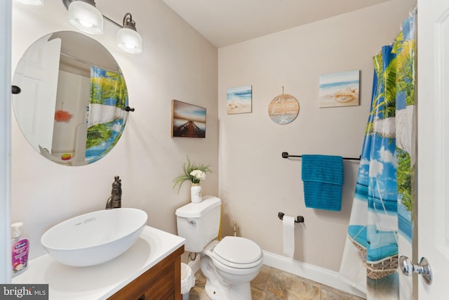 bathroom featuring baseboards, toilet, vanity, and stone finish floor