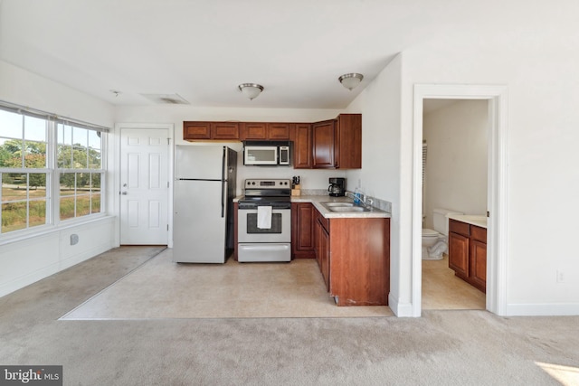 kitchen with a sink, light countertops, appliances with stainless steel finishes, light carpet, and brown cabinets
