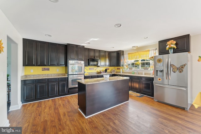 kitchen featuring light stone countertops, wood-type flooring, appliances with stainless steel finishes, a center island, and dark brown cabinetry