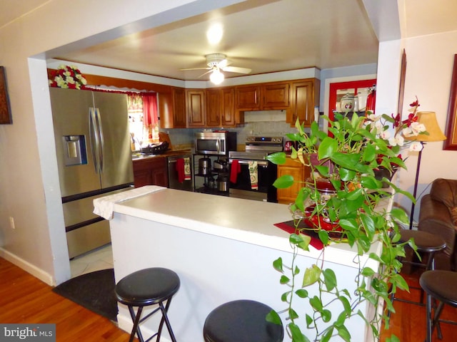 kitchen with stainless steel appliances, kitchen peninsula, decorative backsplash, ceiling fan, and light hardwood / wood-style floors