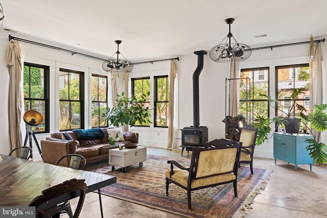 living room with concrete floors, a wood stove, a notable chandelier, and plenty of natural light