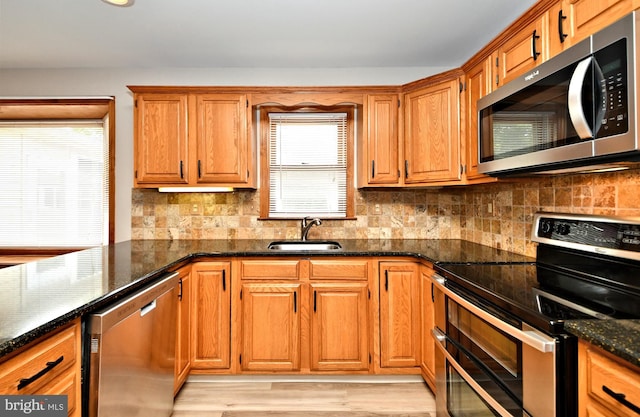 kitchen featuring appliances with stainless steel finishes, tasteful backsplash, light wood-type flooring, dark stone counters, and sink