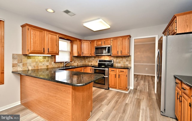 kitchen with light hardwood / wood-style flooring, kitchen peninsula, appliances with stainless steel finishes, and sink