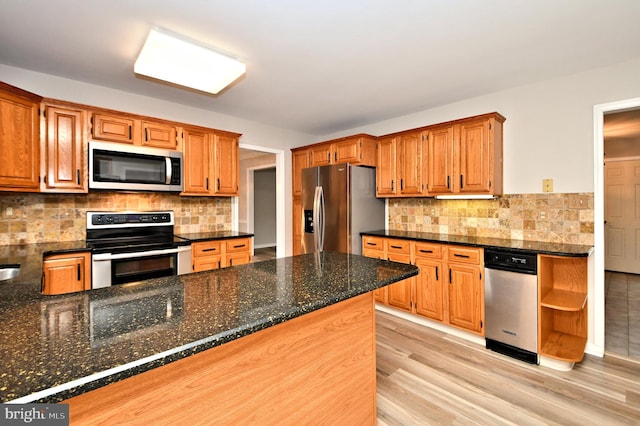 kitchen with light wood-type flooring, kitchen peninsula, decorative backsplash, stainless steel appliances, and dark stone countertops