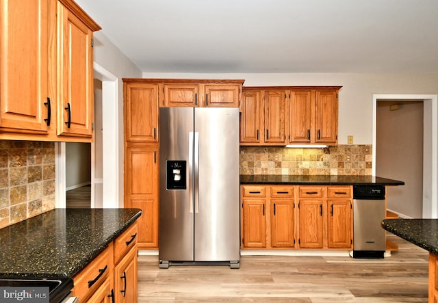 kitchen with dark stone countertops, light hardwood / wood-style floors, tasteful backsplash, and stainless steel fridge