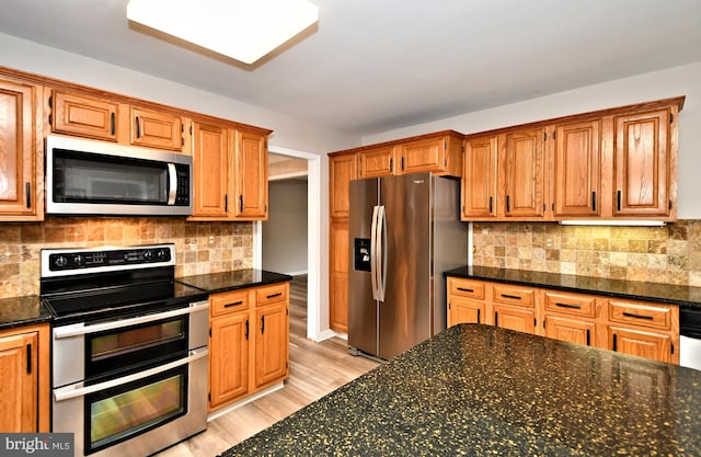 kitchen with appliances with stainless steel finishes, backsplash, light wood-type flooring, and dark stone counters