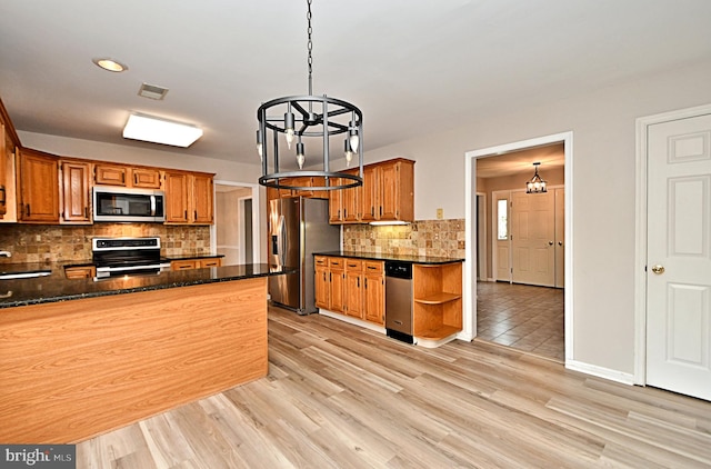 kitchen featuring light wood-type flooring, a notable chandelier, kitchen peninsula, stainless steel appliances, and decorative light fixtures