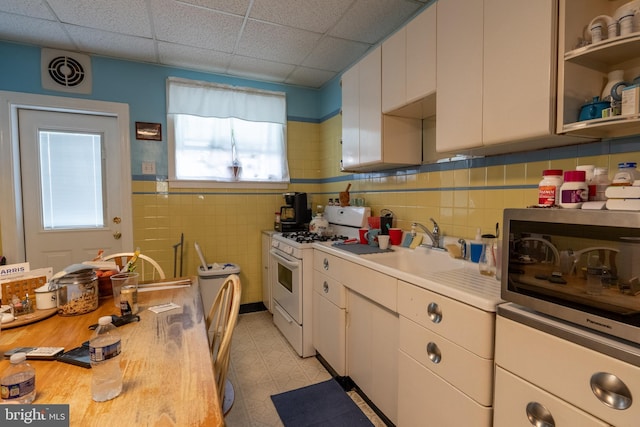 kitchen featuring white cabinets, a drop ceiling, white gas range, and sink