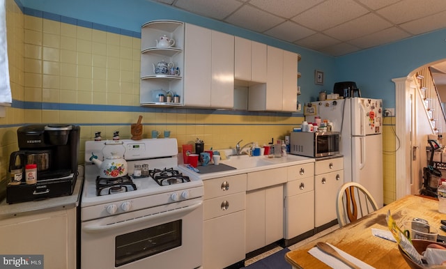 kitchen featuring decorative backsplash, a drop ceiling, white appliances, sink, and white cabinetry