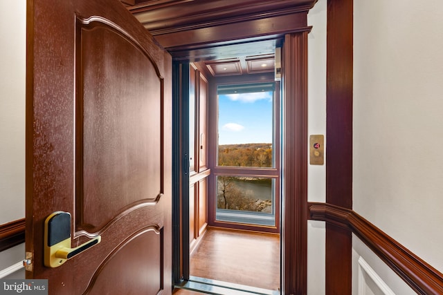 doorway to outside featuring beamed ceiling, wood-type flooring, elevator, and crown molding