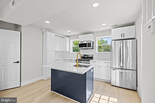 kitchen with appliances with stainless steel finishes, light hardwood / wood-style floors, an island with sink, and white cabinets