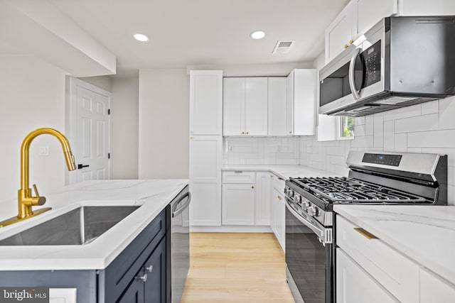 kitchen featuring light wood-type flooring, sink, white cabinetry, stainless steel appliances, and light stone countertops