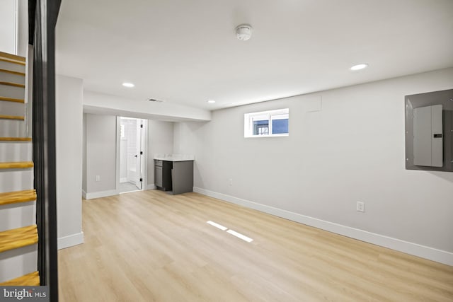 basement featuring electric panel and light hardwood / wood-style flooring