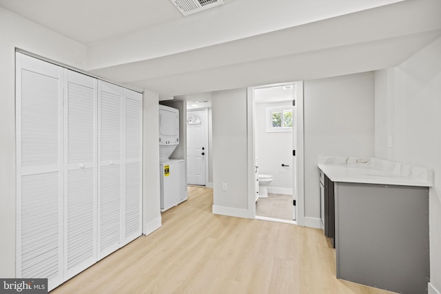 interior space featuring stacked washer / dryer, connected bathroom, light hardwood / wood-style flooring, and a closet