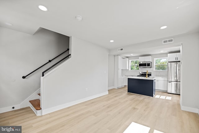 interior space featuring white cabinetry, a kitchen island, light hardwood / wood-style flooring, backsplash, and appliances with stainless steel finishes