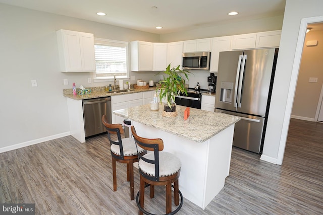 kitchen with appliances with stainless steel finishes, a kitchen island, white cabinetry, and wood-type flooring