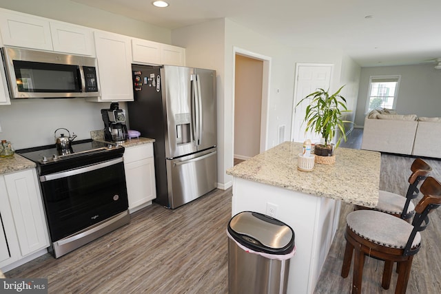 kitchen featuring a center island, appliances with stainless steel finishes, light stone countertops, white cabinetry, and dark wood-type flooring