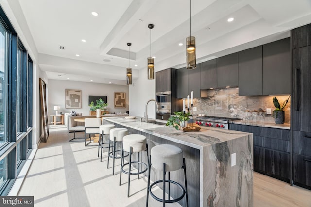 kitchen featuring hanging light fixtures, sink, tasteful backsplash, a large island, and light wood-type flooring