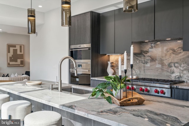 kitchen with tasteful backsplash, light stone counters, stainless steel appliances, decorative light fixtures, and sink