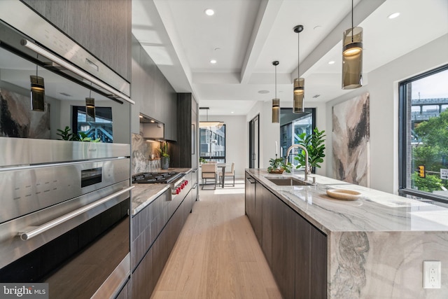 kitchen featuring sink, pendant lighting, light wood-type flooring, appliances with stainless steel finishes, and a large island with sink