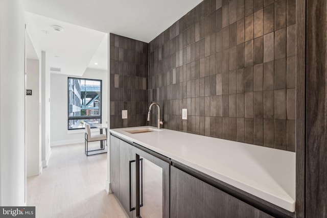 kitchen with light wood-type flooring, tile walls, sink, and dark brown cabinets