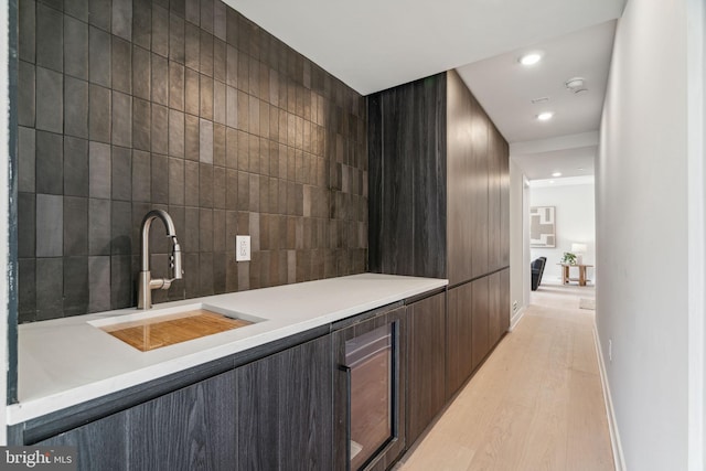 bar featuring dark brown cabinets, sink, light hardwood / wood-style flooring, and tile walls