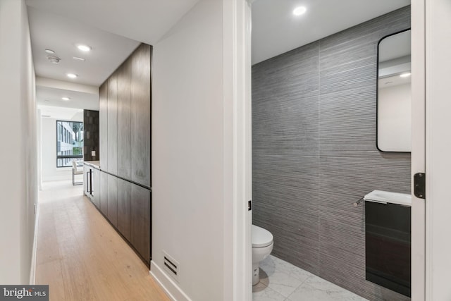 bathroom featuring toilet, vanity, wood-type flooring, and tile walls