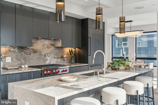 kitchen with a kitchen bar, sink, backsplash, light stone countertops, and pendant lighting