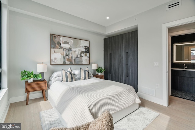 bedroom with connected bathroom and light wood-type flooring