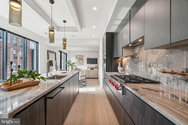 kitchen with light hardwood / wood-style floors, stainless steel gas cooktop, sink, light stone countertops, and decorative light fixtures