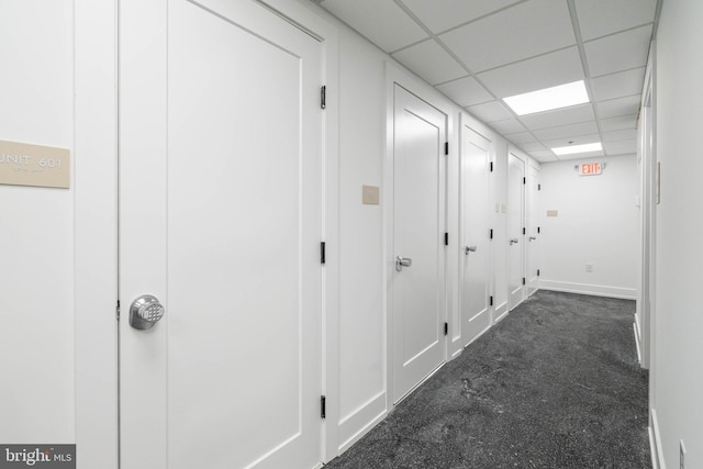 hallway featuring a drop ceiling and dark colored carpet