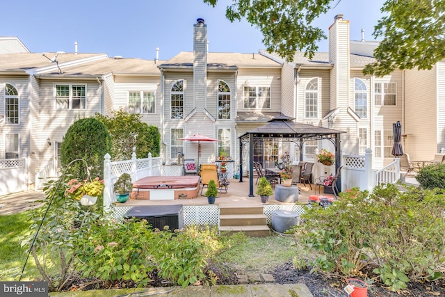 rear view of property featuring a hot tub, a deck, and a gazebo