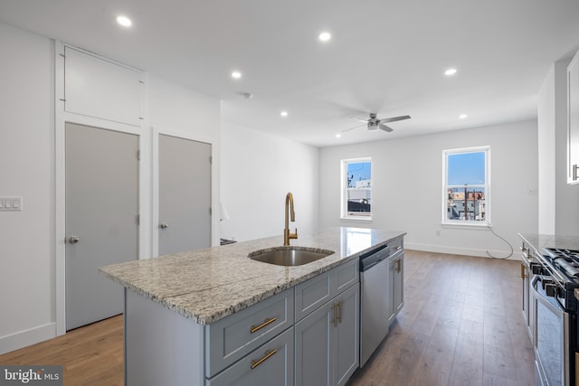 kitchen with a center island with sink, stainless steel appliances, sink, hardwood / wood-style flooring, and ceiling fan