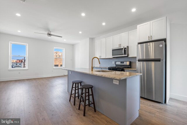 kitchen featuring a kitchen island with sink, light hardwood / wood-style flooring, stainless steel appliances, ceiling fan, and white cabinets