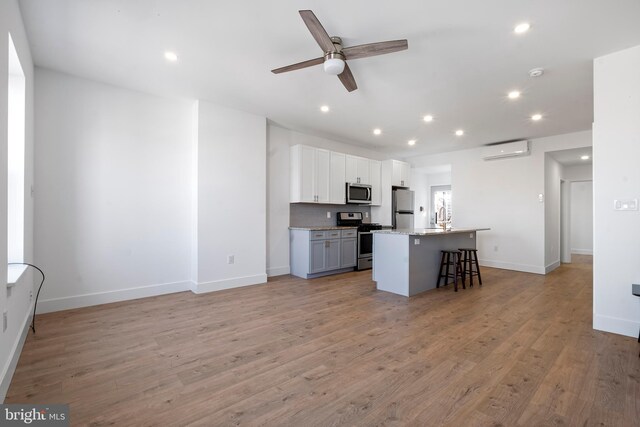 kitchen featuring a center island with sink, light hardwood / wood-style flooring, appliances with stainless steel finishes, a kitchen bar, and ceiling fan