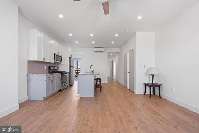 kitchen featuring a breakfast bar area, light hardwood / wood-style flooring, an island with sink, stainless steel appliances, and white cabinets