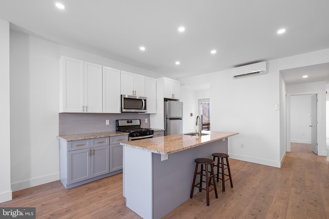 kitchen featuring a center island with sink, a kitchen bar, stainless steel appliances, sink, and light wood-type flooring