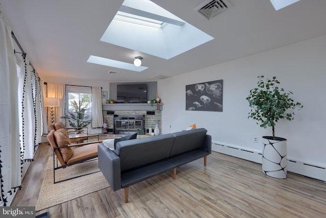 living room featuring light hardwood / wood-style floors, a stone fireplace, a baseboard radiator, and a skylight