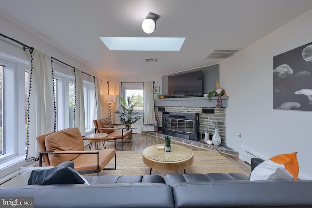 living room with a skylight, a stone fireplace, a baseboard heating unit, and hardwood / wood-style flooring