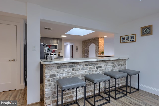 bar featuring light hardwood / wood-style floors, appliances with stainless steel finishes, and a skylight