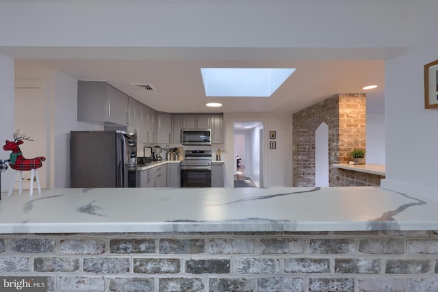 kitchen with gray cabinets, kitchen peninsula, appliances with stainless steel finishes, and a skylight