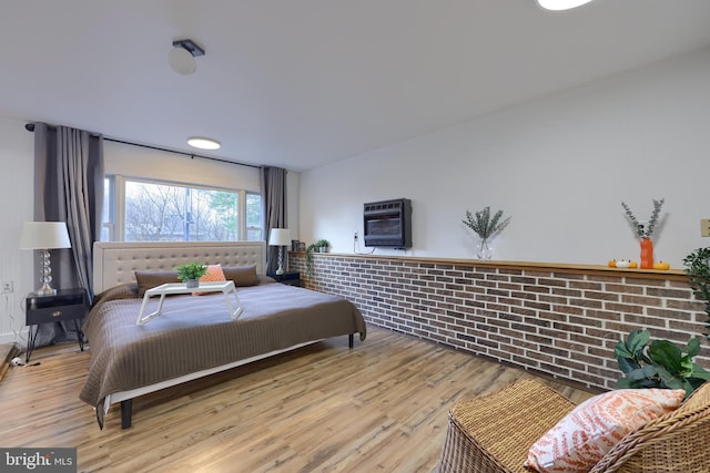 bedroom with light hardwood / wood-style floors, brick wall, and heating unit