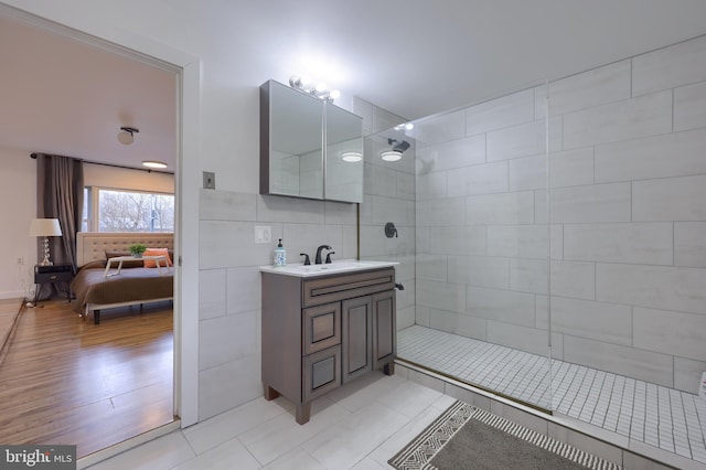 bathroom featuring hardwood / wood-style floors, vanity, tile walls, and tiled shower