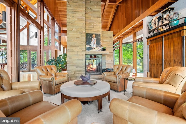 living room with a high ceiling, wood walls, beamed ceiling, and a stone fireplace